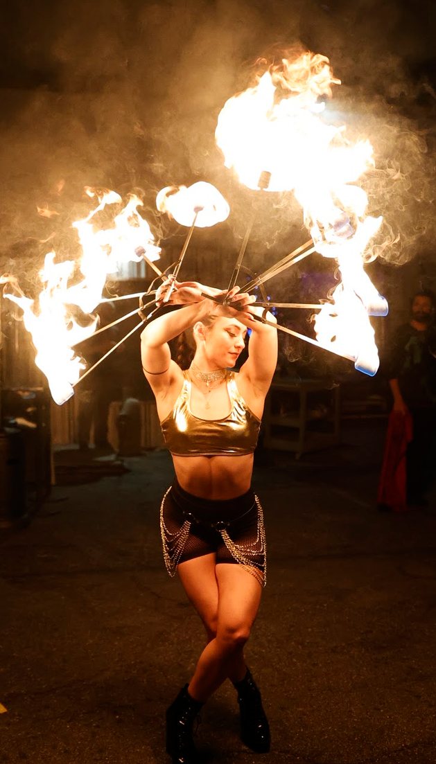 Performer holding a crown of lit fire fans over her head
