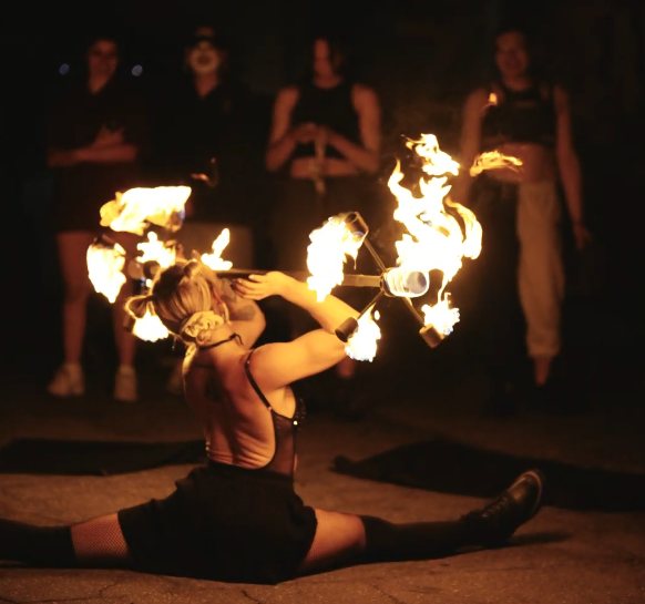 Performer in the splits with lit fire fans crossed behind her head